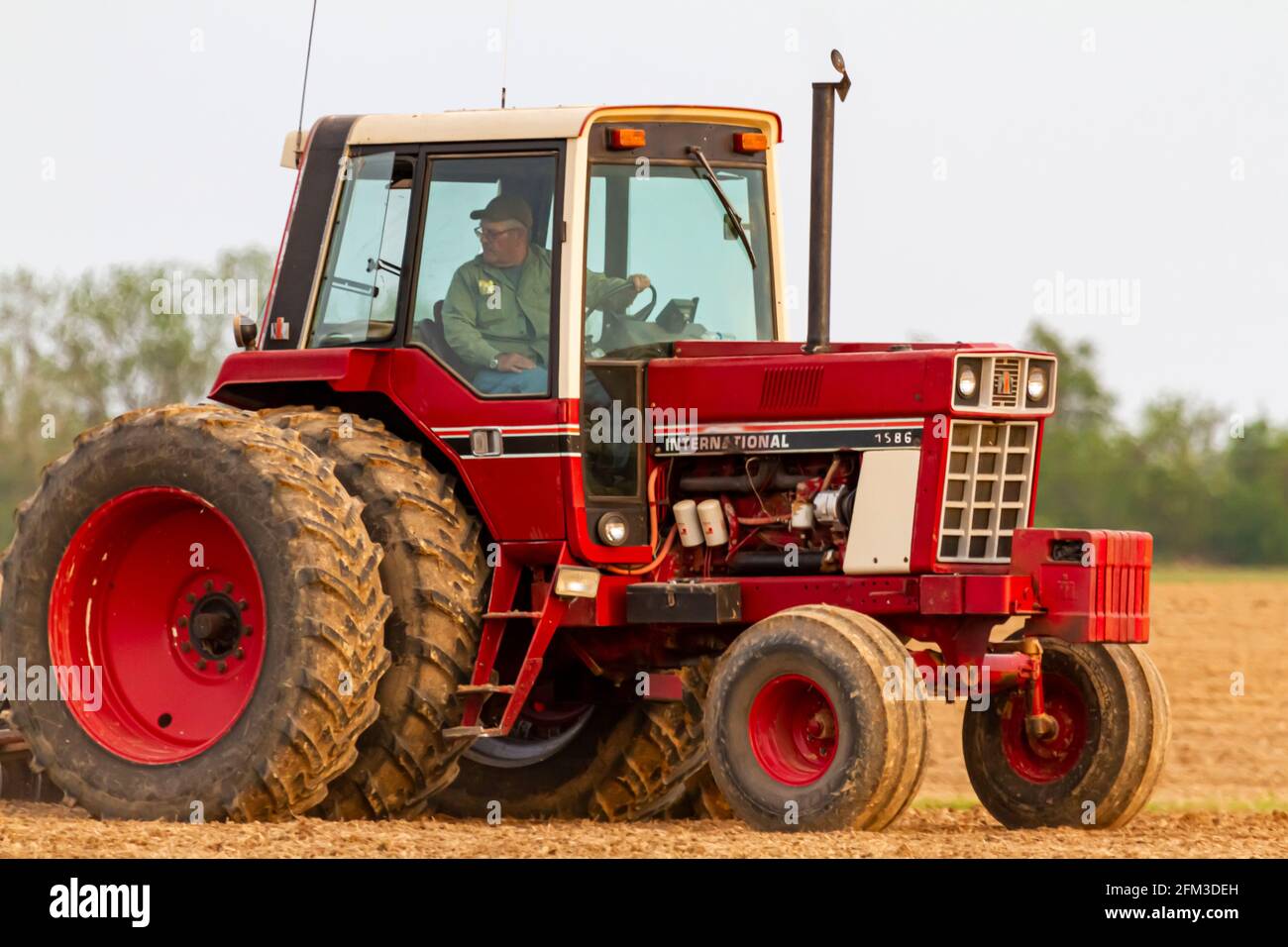 Chestertown, MD, USA 05-02-2021: Primo piano immagine isolata di un trattore internazionale 1586 a sei ruote rosse con cabina che arava un campo agricolo vuoto i Foto Stock