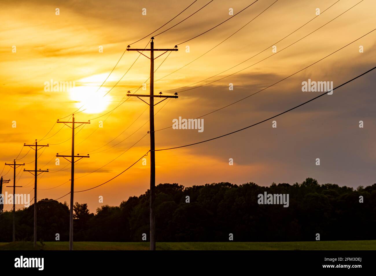 Silhouette di pali di servizio che trasportano l'elettricità di alta tensione lungo una strada in un'area rurale. Tramonto, alba con cielo rosso arancio nuvoloso e. Foto Stock