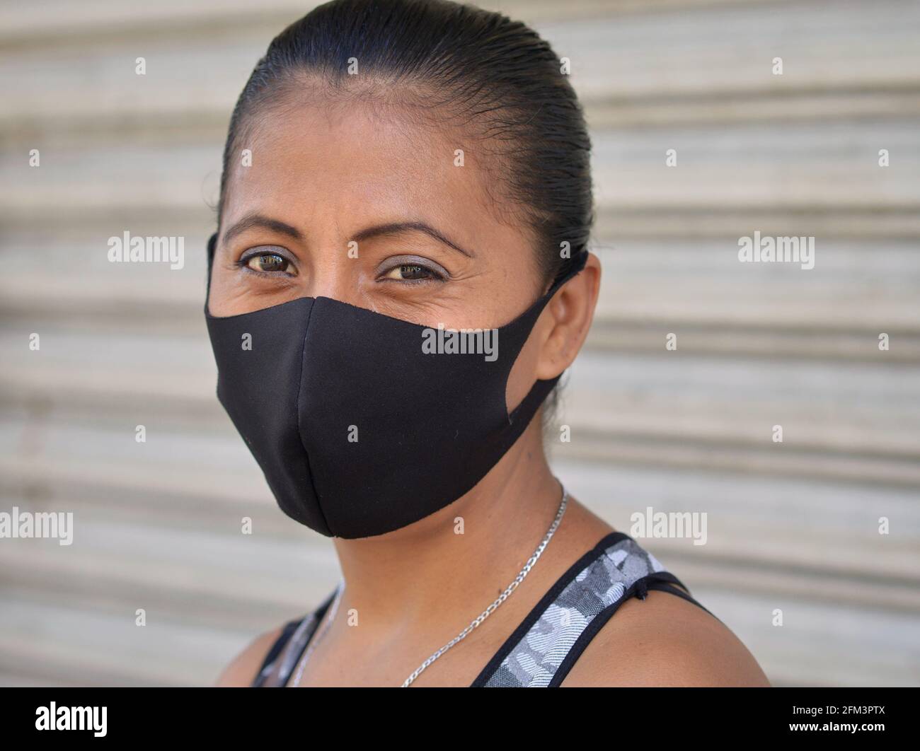 La donna messicana di mezza età con gli occhi marroni, indossa una maschera facciale non medica in tessuto nero durante la pandemia globale di coronavirus in corso. Foto Stock