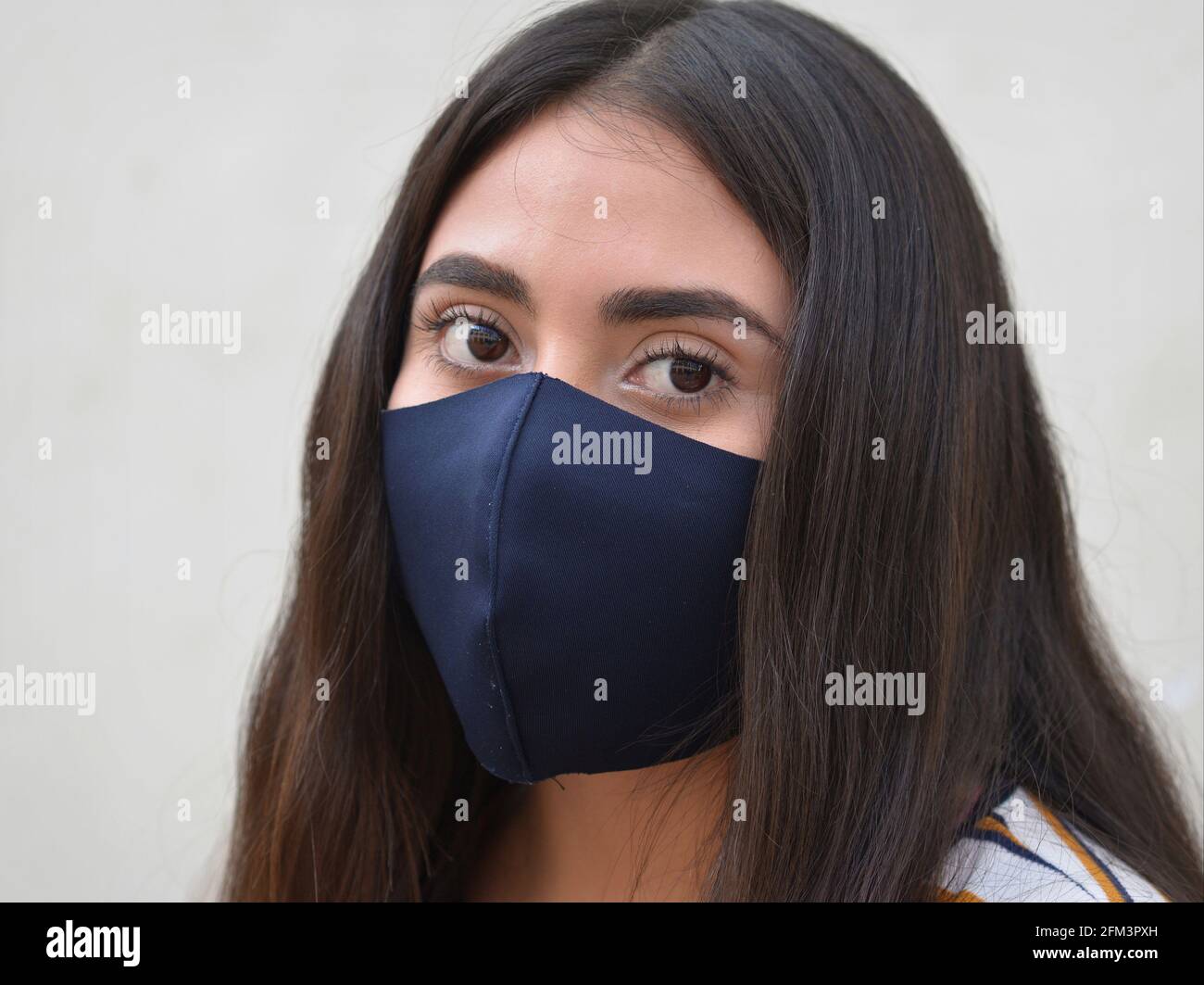 Giovane donna caucasica latina con grandi occhi marroni e capelli lunghi indossa una maschera nera lavabile non medica durante la pandemia globale del coronavirus. Foto Stock