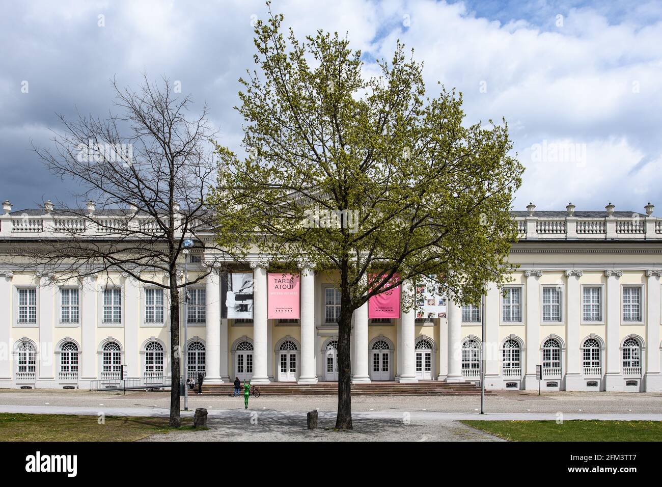 Kassel, Germania. 03 maggio 2021. Un albero di quercia piantato dall'artista d'azione Joseph Beuys si trova di fronte all'edificio del museo Fridericianum. L'azione '7000 querce' dell'artista Joseph Beuys, in cui gli alberi sono stati piantati a Kassel con pietre di basalto accanto a loro, è stata iniziata nel 1982 come parte di Documenta 7 e proseguita fino a quando l'ultimo albero è stato piantato nel 1987. L'artista del secolo Beuys è nato 100 anni fa il 12 maggio. Credit: Swen Pförtner/dpa/Alamy Live News Foto Stock