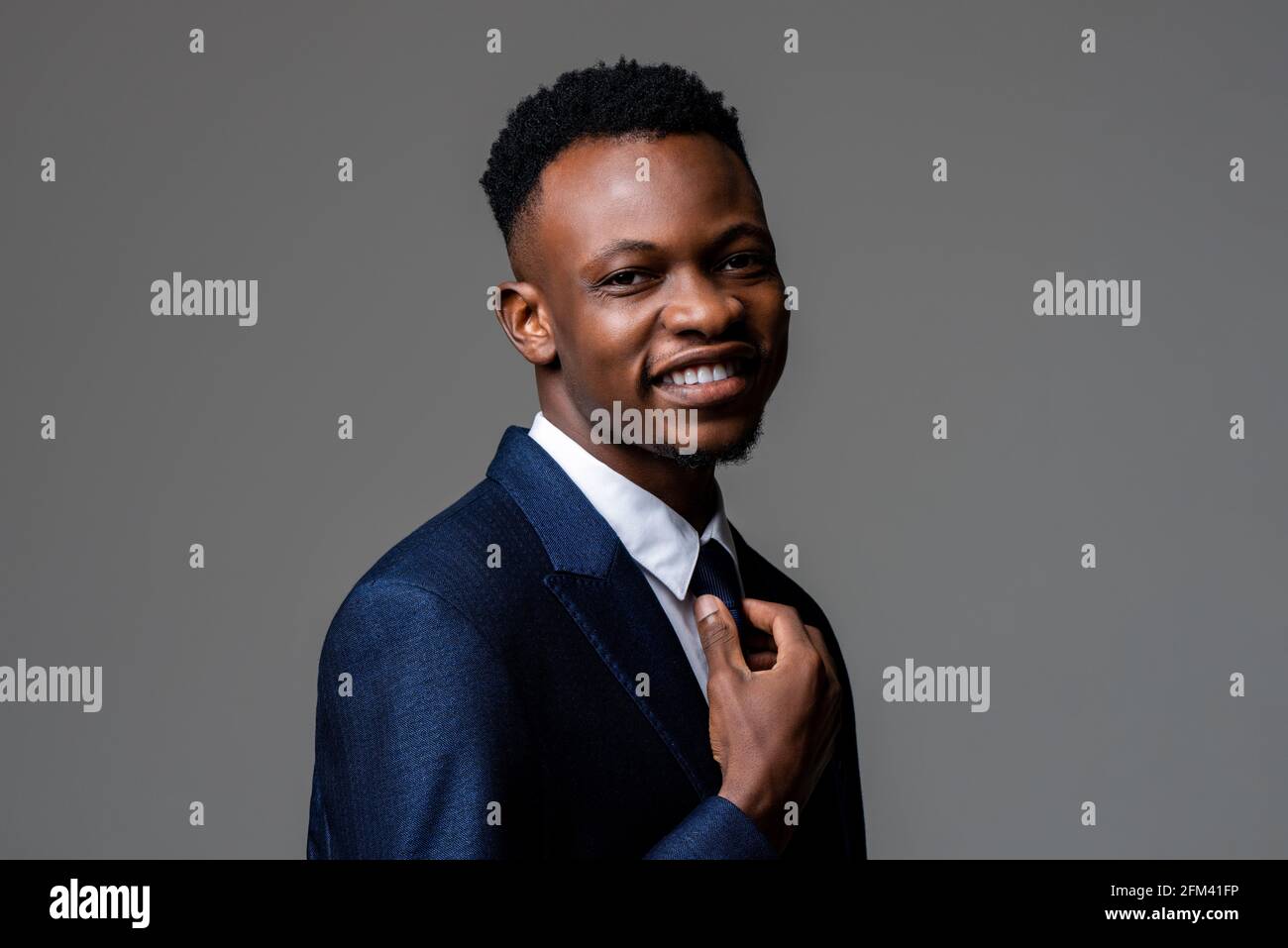 Giovane sorridente allegro bell'uomo africano che indossa una tuta da lavoro formale in studio grigio sfondo isolato Foto Stock
