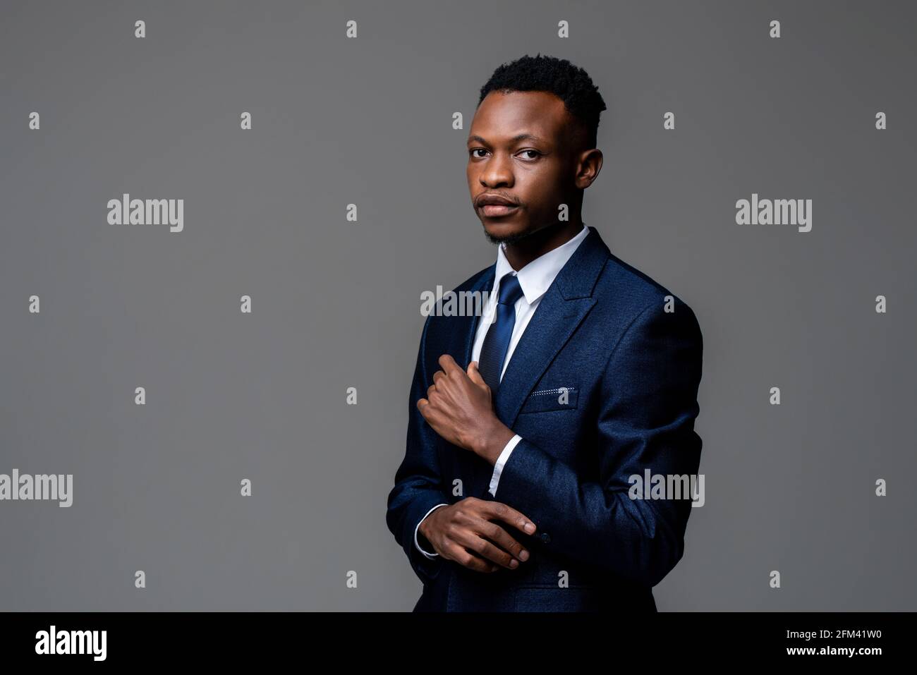 Ritratto di un giovane bell'uomo africano che indossa un abito da lavoro formale guardando la telecamera isolata su sfondo grigio dello studio Foto Stock