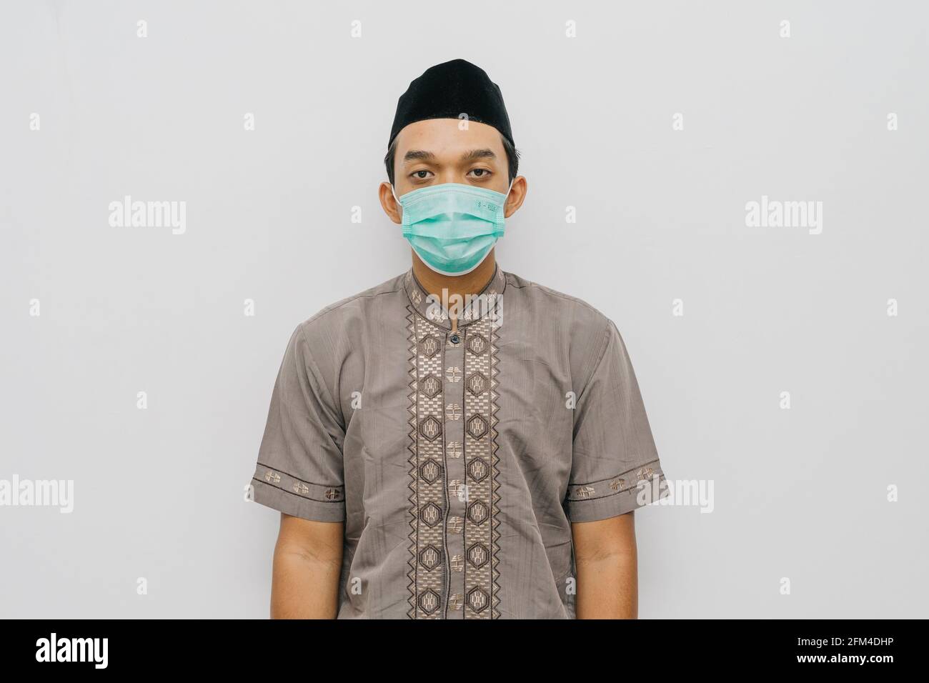 Ritratto di uomo indonesiano indossa maschera medica, camicia musulmana e peci o songkok per fare la preghiera salat Foto Stock