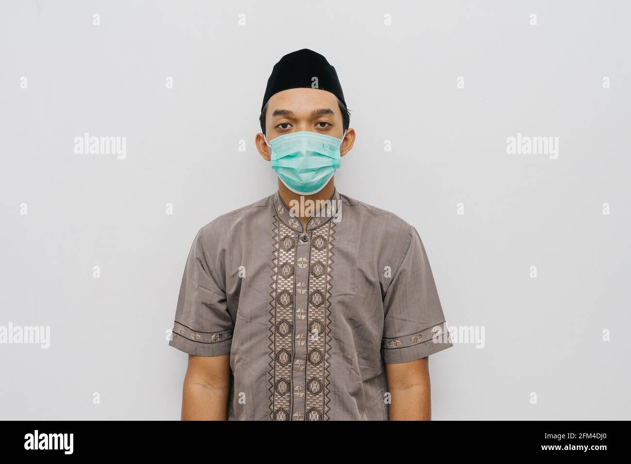 Ritratto di uomo indonesiano indossa maschera medica, camicia musulmana e peci o songkok per fare la preghiera salat Foto Stock