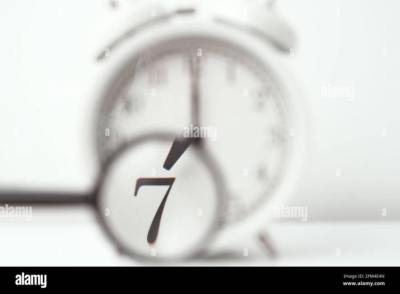 La lente di ingrandimento punta al numero 7 sulla sveglia retrò sull'orologio bianco. Concetto di mattina Foto Stock