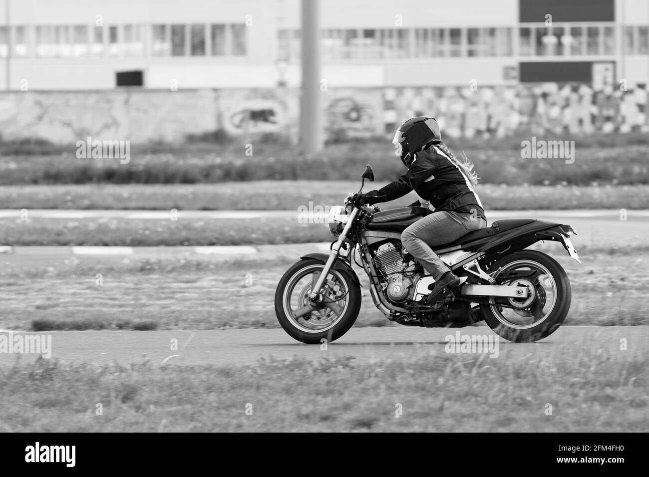 Ulyanovsk, Russia - 10 giugno 2017. La ragazza in una giacca nera e pantaloni grigi gareggia su una moto. Sfocatura del movimento. Immagine in bianco e nero. Foto Stock