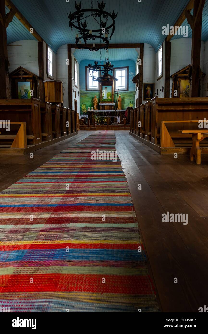 Interno di una vecchia chiesa in legno. Soffitti blu, pareti bianche, banchi di legno, sculture folcloristiche sull'altare. Crepuscolo naturale per una luce soffusa. Foto Stock