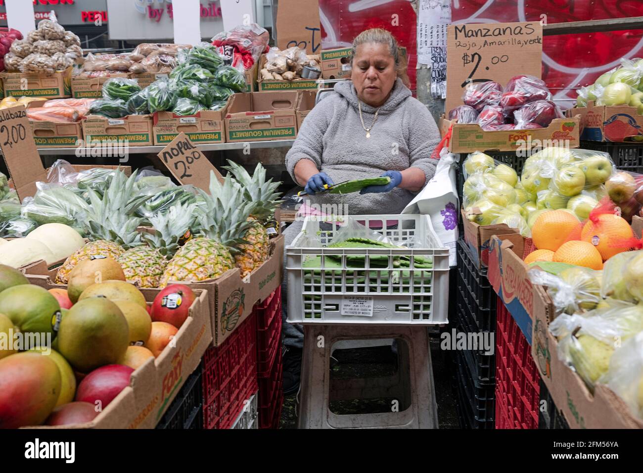 Una donna che gestisce uno stand di frutta e verdura sotto l'el in Corona, strips una foglia di cactus. A New York. Foto Stock