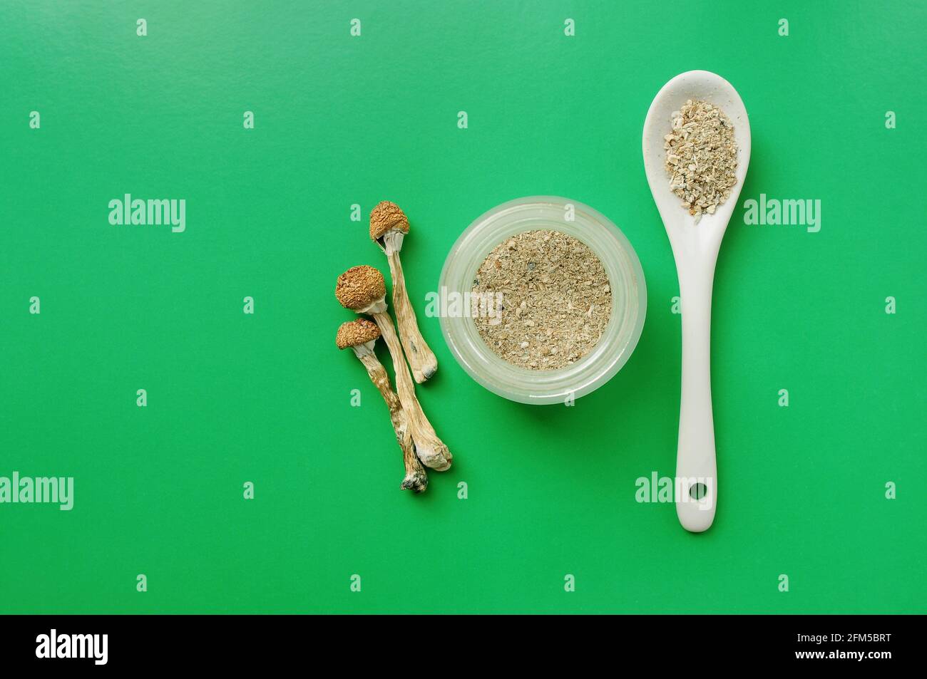 Concetto di microdosaggio. Funghi psilocibin asciutti su sfondo verde. Supplemento biologico naturale. Uso medico. Viaggio magico psichedelico. Foto Stock