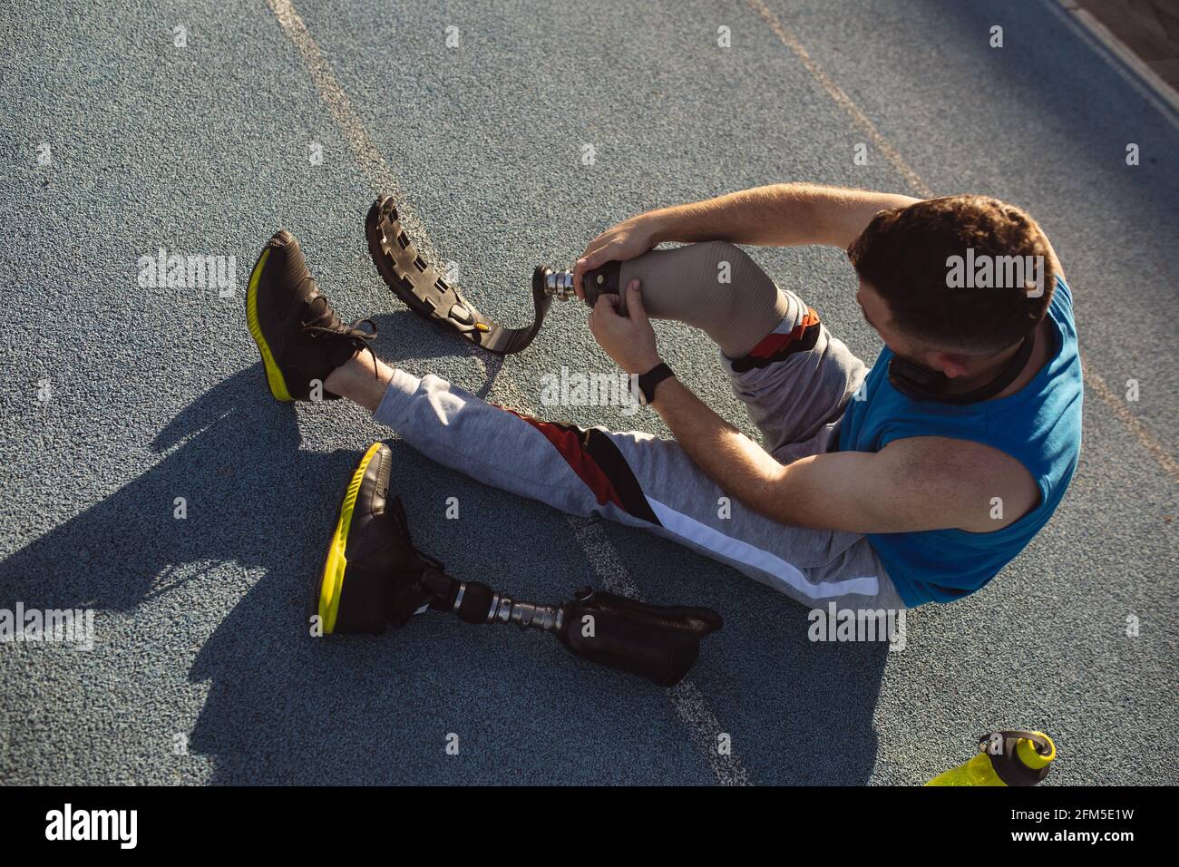Atleta maschio caucasico che fissa la gamba protesica mentre si siede pista da corsa nello stadio Foto Stock