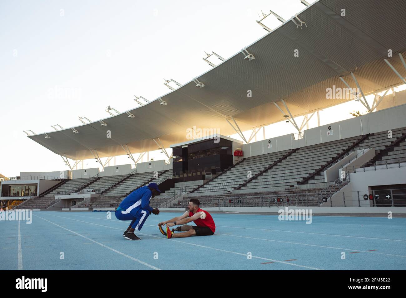 Allenatore africano americano maschio che istruisce l'atleta maschio caucasico con la protesi gamba su pista Foto Stock