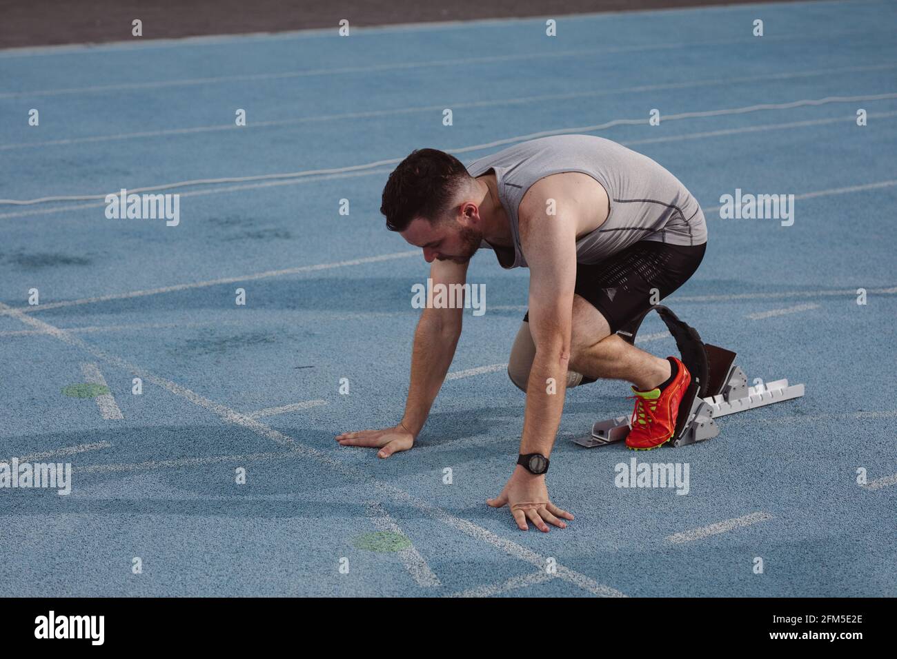 Atleta maschio caucasico con gamba protesica in posizione di partenza per in pista Foto Stock