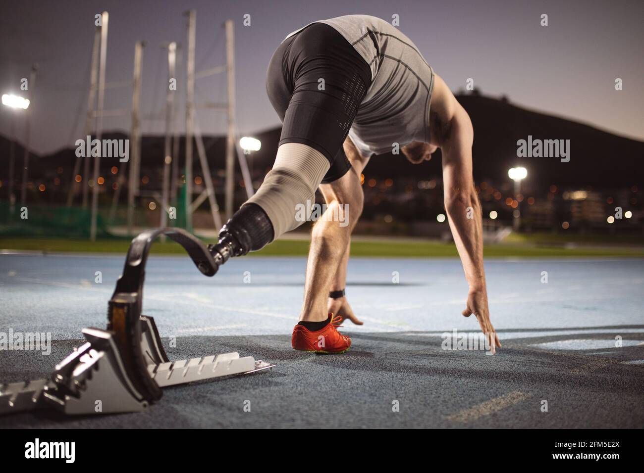 Atleta maschio caucasico con gamba protesica in posizione di partenza per corsa in pista di notte Foto Stock