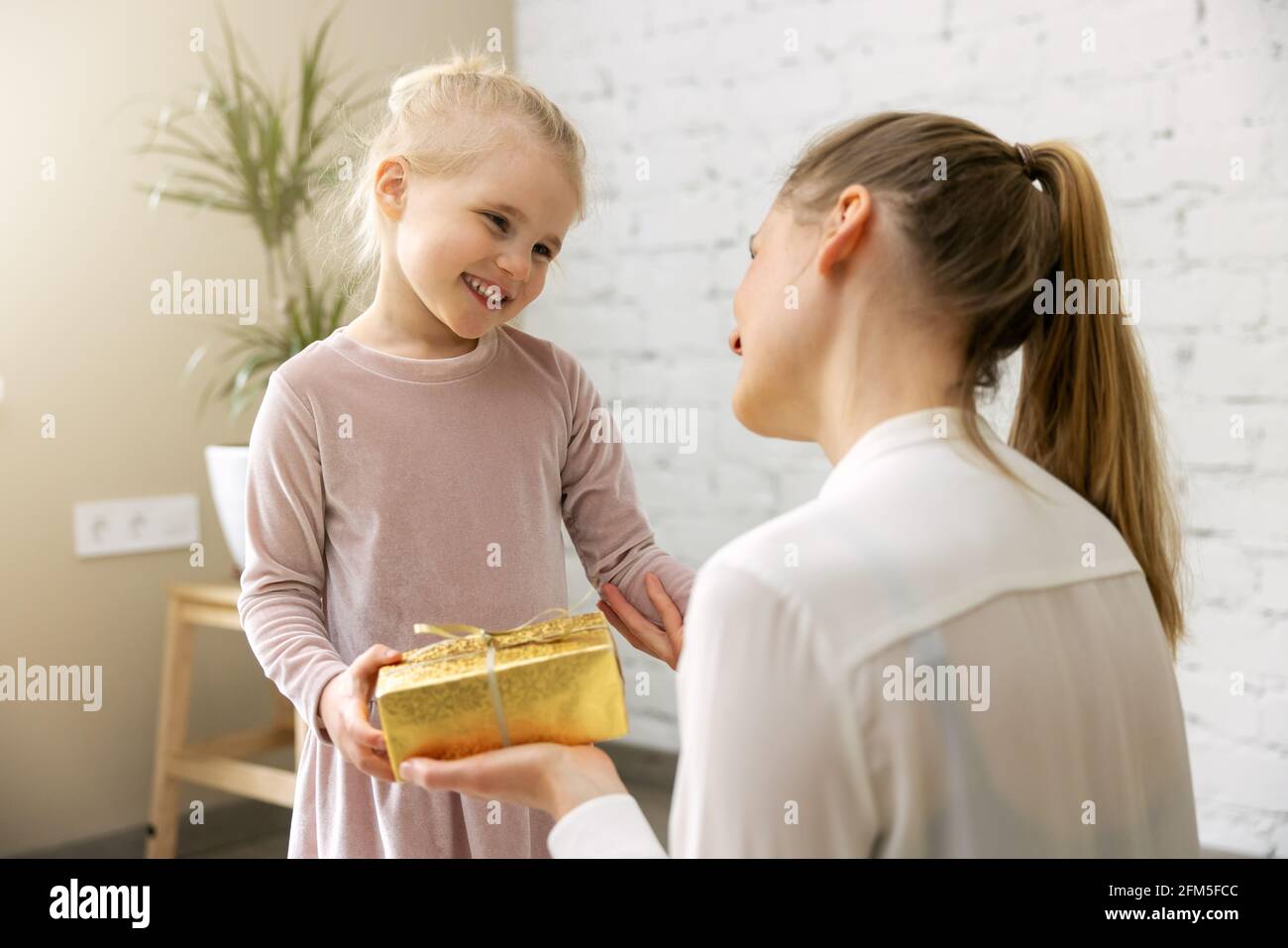 figlia sorridente che dà scatola del regalo alla sua mamma a casa. compleanno o concetto di giorno delle madri Foto Stock