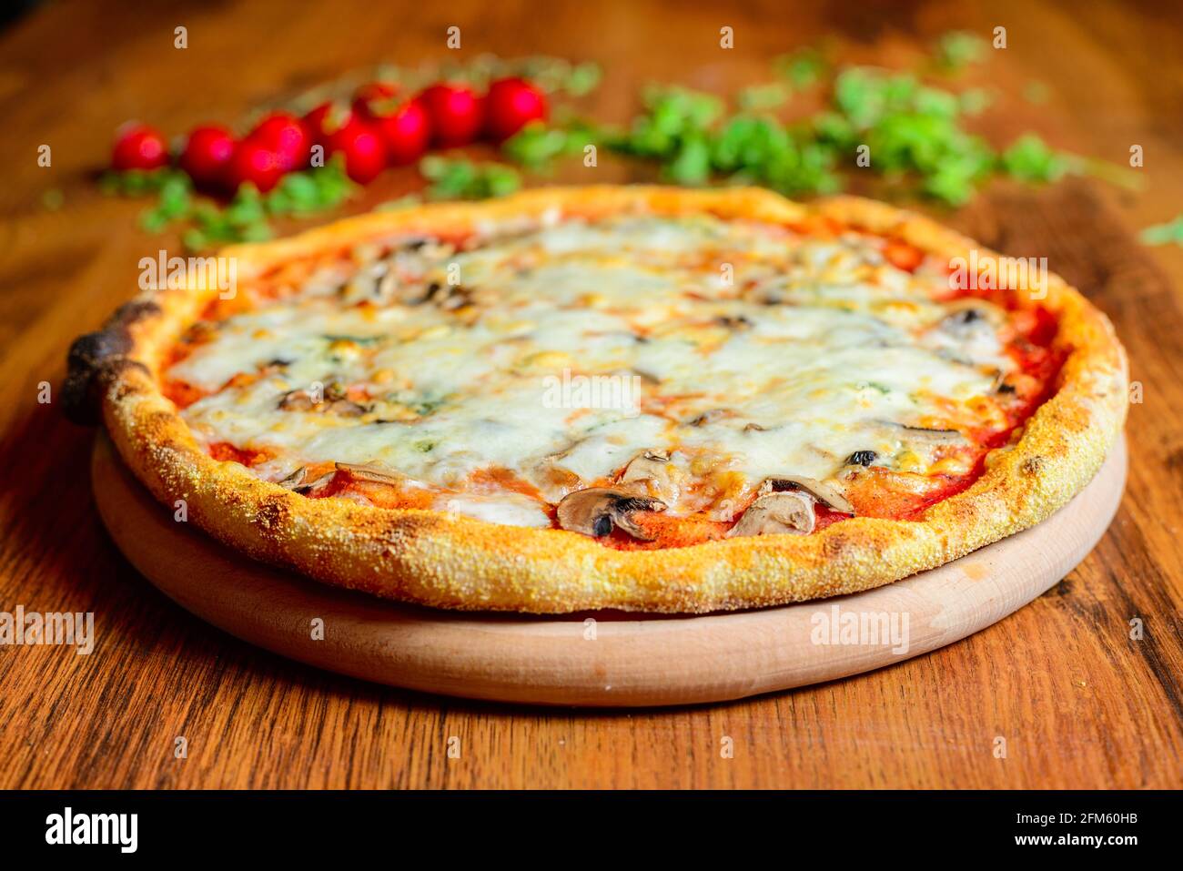 Primo piano vista ad angolo acuto della pizza italiana Margherita posta su tavolo di legno con arugula decorativa e pomodori ciliegini sullo sfondo. Foto Stock