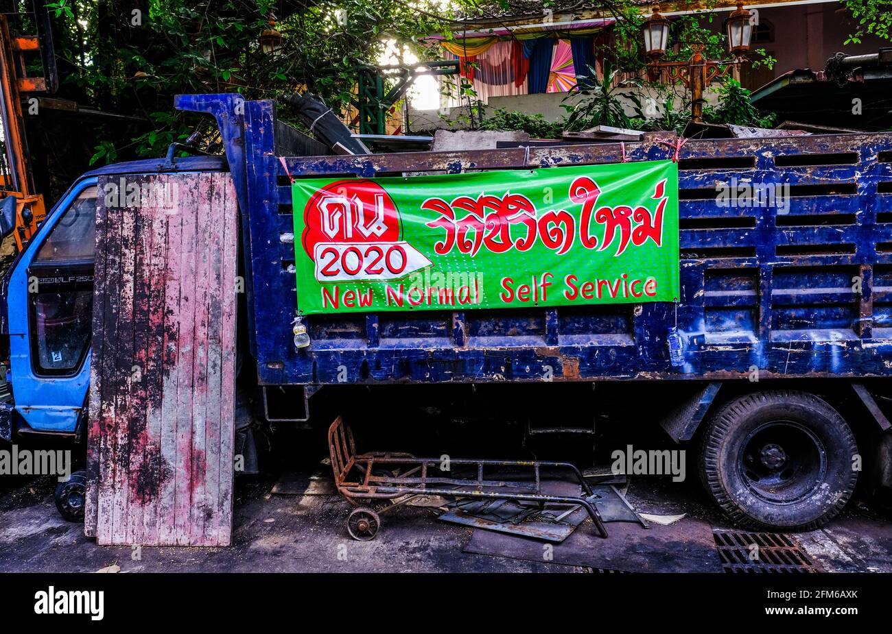 Un vecchio camion blu, che immagazzina le parti vecchie dell'automobile, mostra un banner che descrive le nuove pratiche normali di vendita durante il Pandemic del Covid a Bangkok, Tailandia. Foto Stock