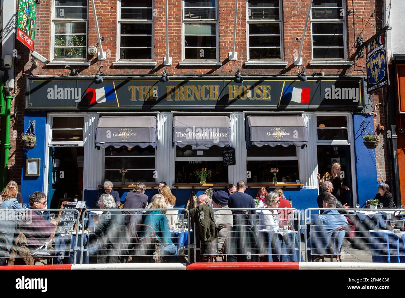 I bevitori si siedono fuori dalla Casa Francese a Soho socialmente distanziati sui tavoli allestiti lungo il marciapiede in un pomeriggio soleggiato, Londra, Regno Unito Foto Stock