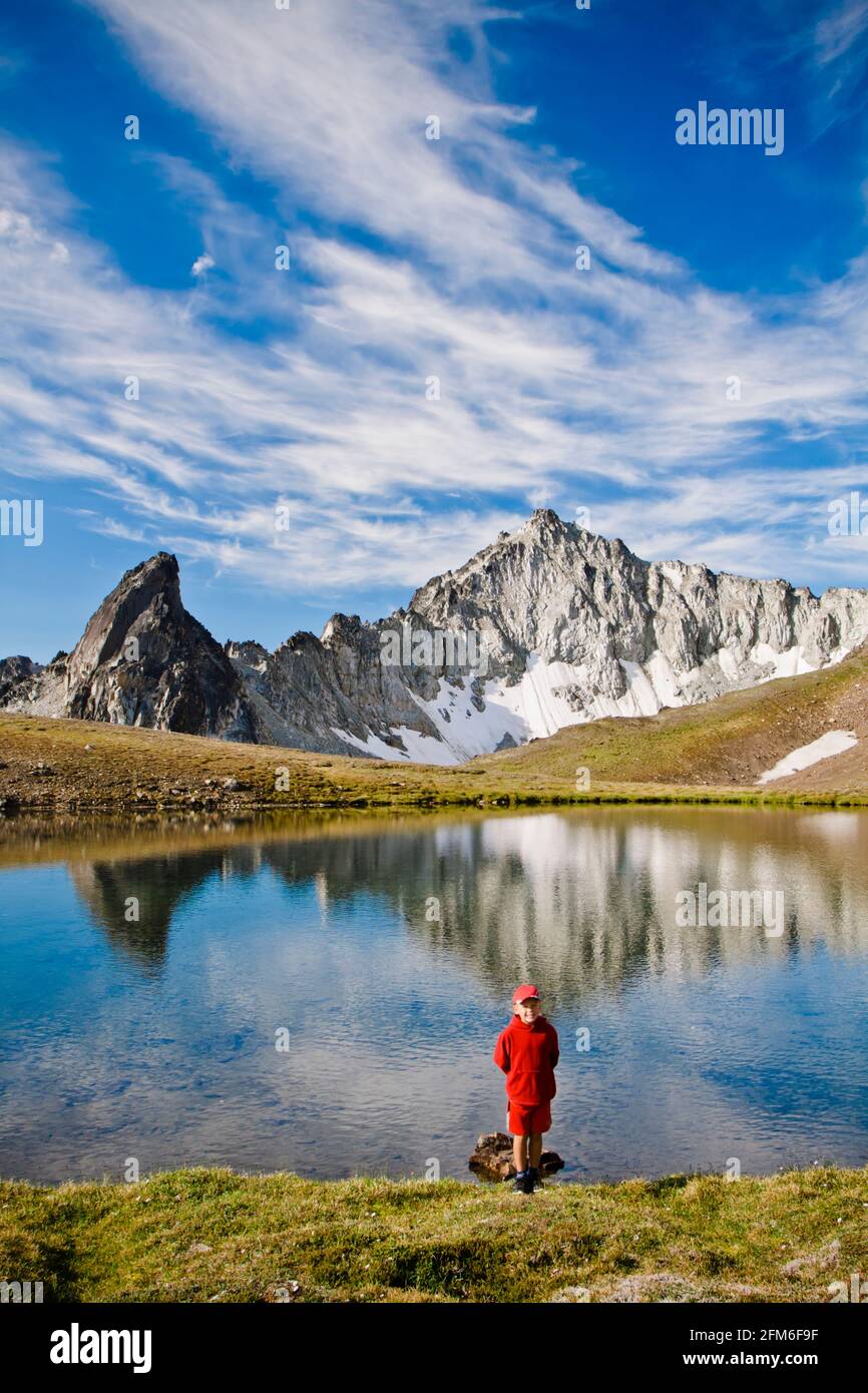 Ragazzo giovane che indossa rosso, in piedi di fronte al lago alpino, cime panoramiche Foto Stock
