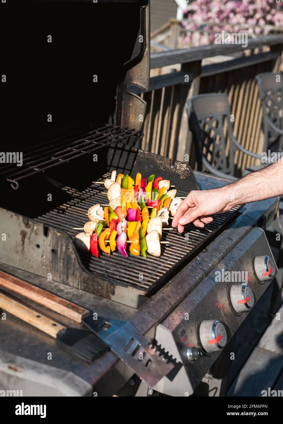 Uomo che mette spiedini di verdure su una griglia a gas barbecue all'aperto. Foto Stock