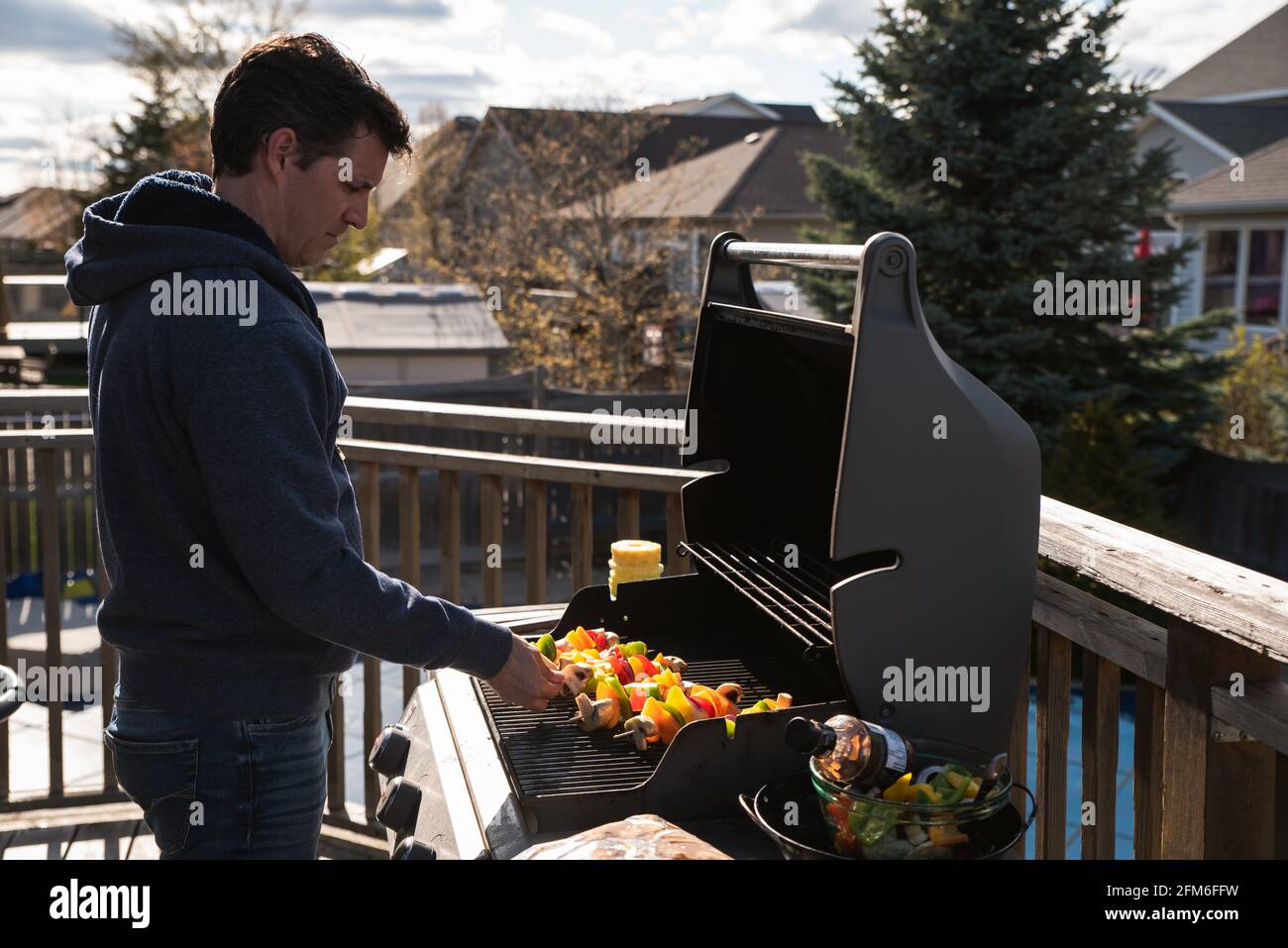 Uomo che mette spiedini di verdure su una griglia a gas barbecue all'aperto. Foto Stock
