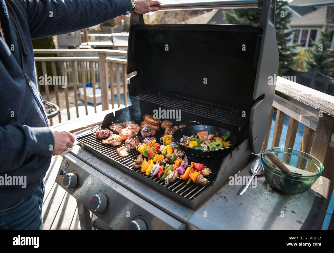 Uomo che grigliano pollo e verdure all'aperto su una griglia a gas barbecue. Foto Stock