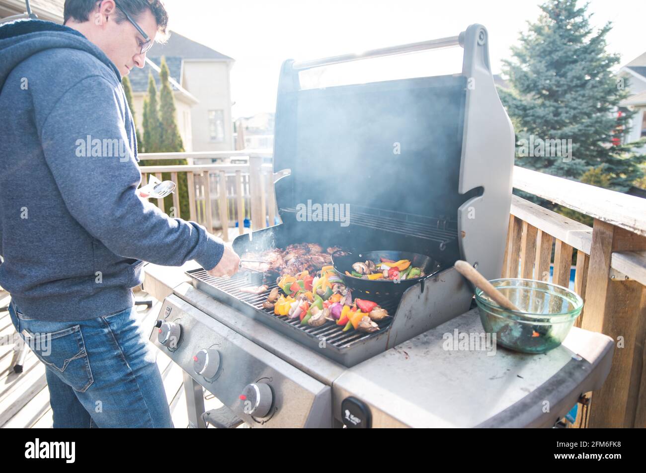 Uomo che grigliano pollo e verdure all'aperto su una griglia a gas barbecue. Foto Stock