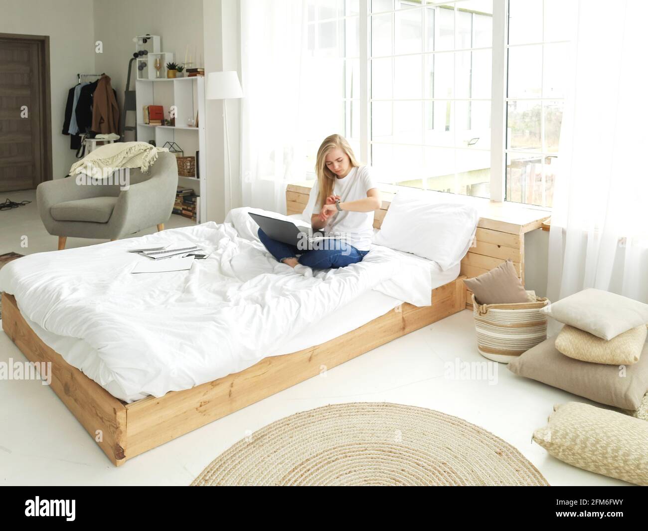 bionda giovane donna seduta sul letto bianco guardando l'orologio Foto Stock
