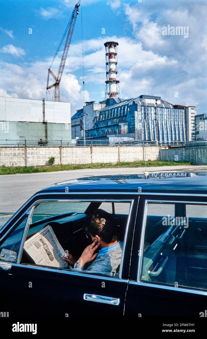 Il conducente dell'ex governo sovietico limousine legge tranquillamente Il giornale di fronte al blocco IV reattore danneggiato Della polvere nucleare di Chernobyl Foto Stock