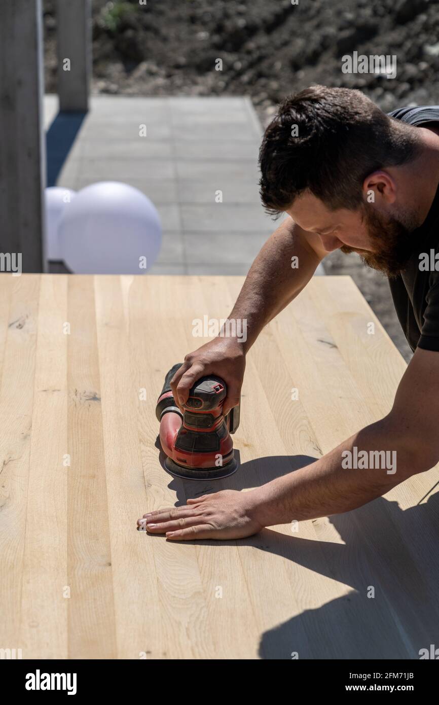 lavoratori edili che utilizzano una smerigliatrice elettrica senza fili per levigare un tavolo in legno massiccio Foto Stock