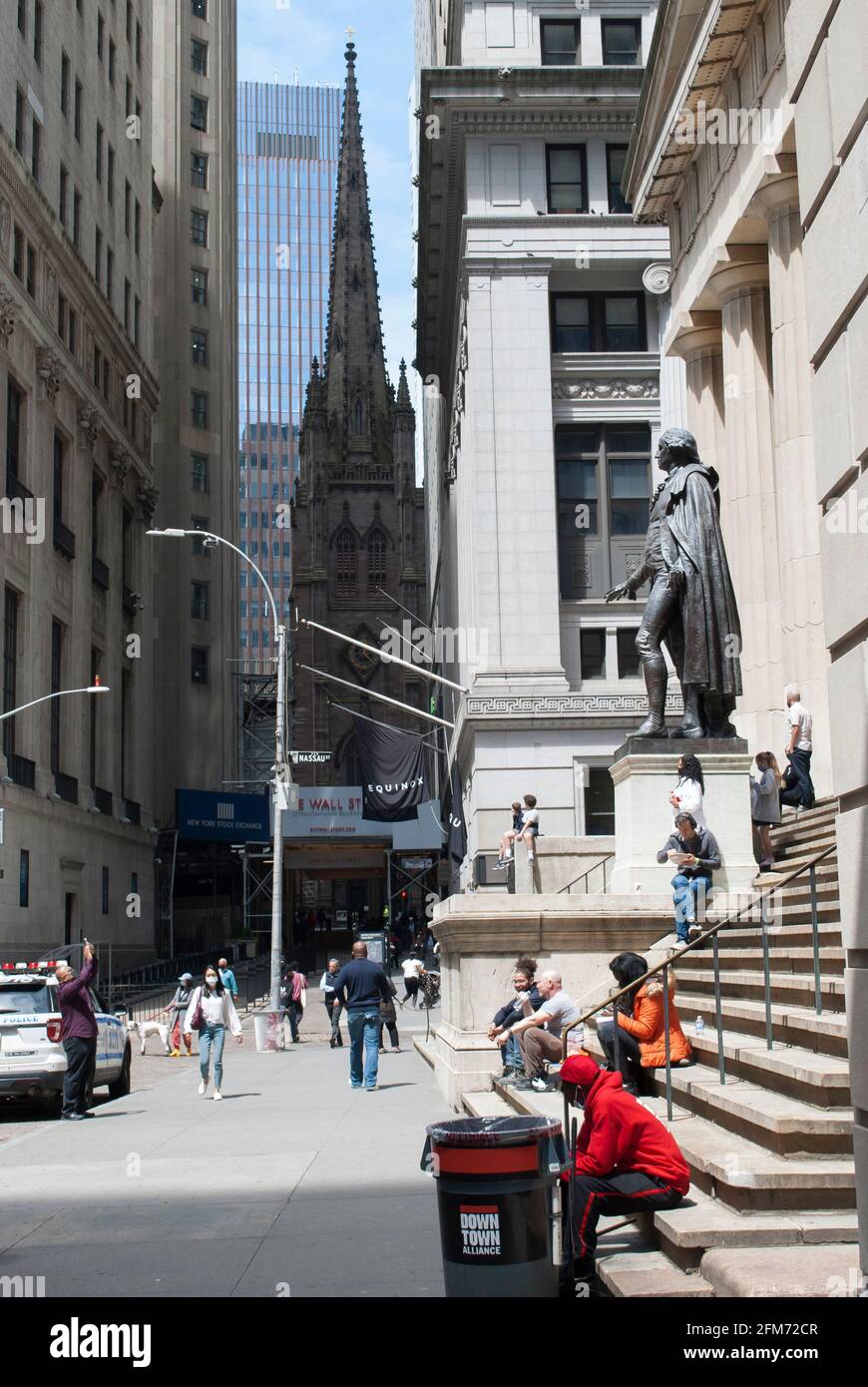 La gente è seduta davanti all'edificio federale su Wall Street, New York. La vista sulla Chiesa della Trinità. Foto Stock
