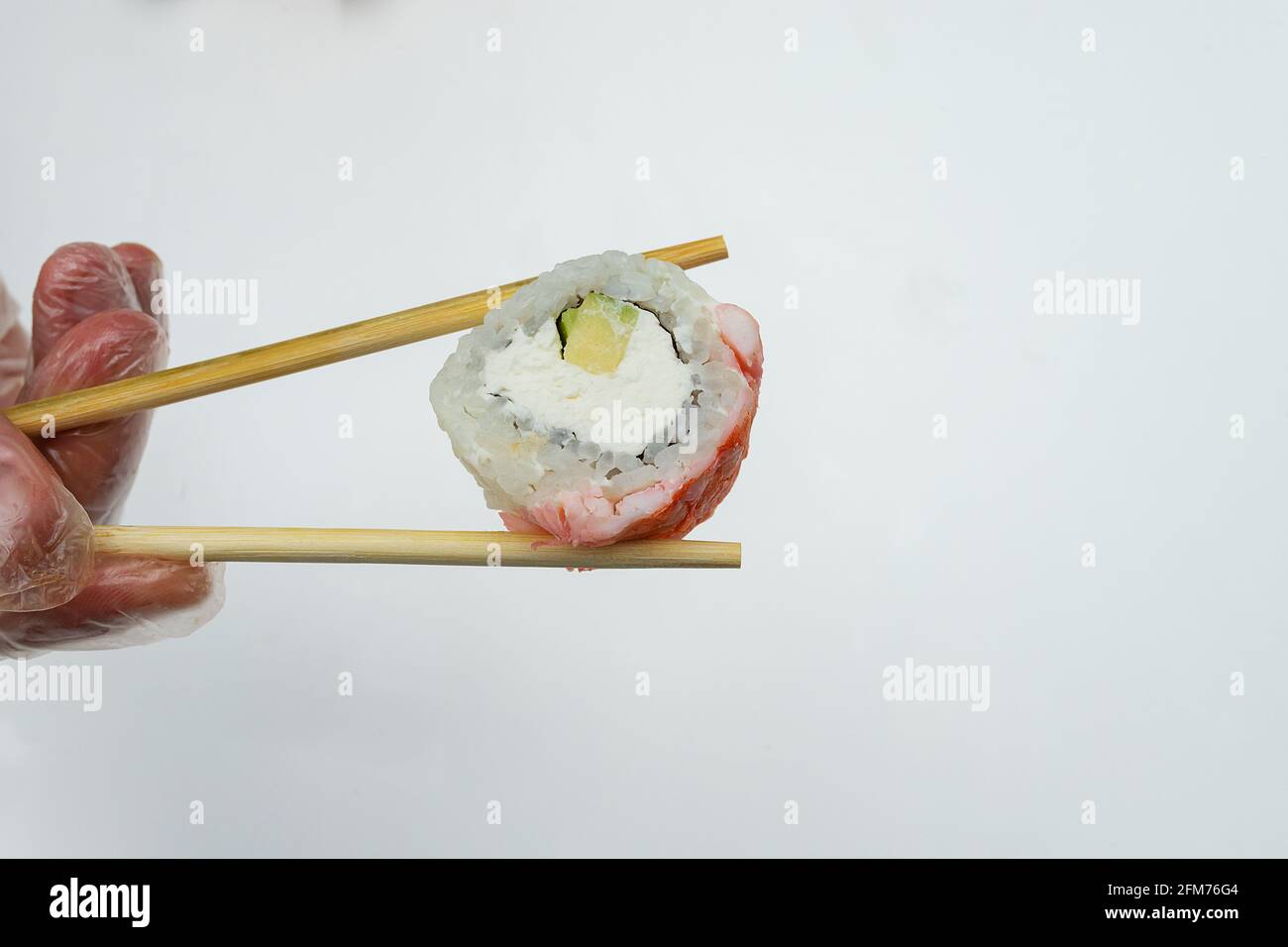 Bastoncini di sushi che tengono a mano, sullo sfondo di una grande porzione di piatti di riso della cucina asiatica, cibo con strumenti tradizionali Foto Stock