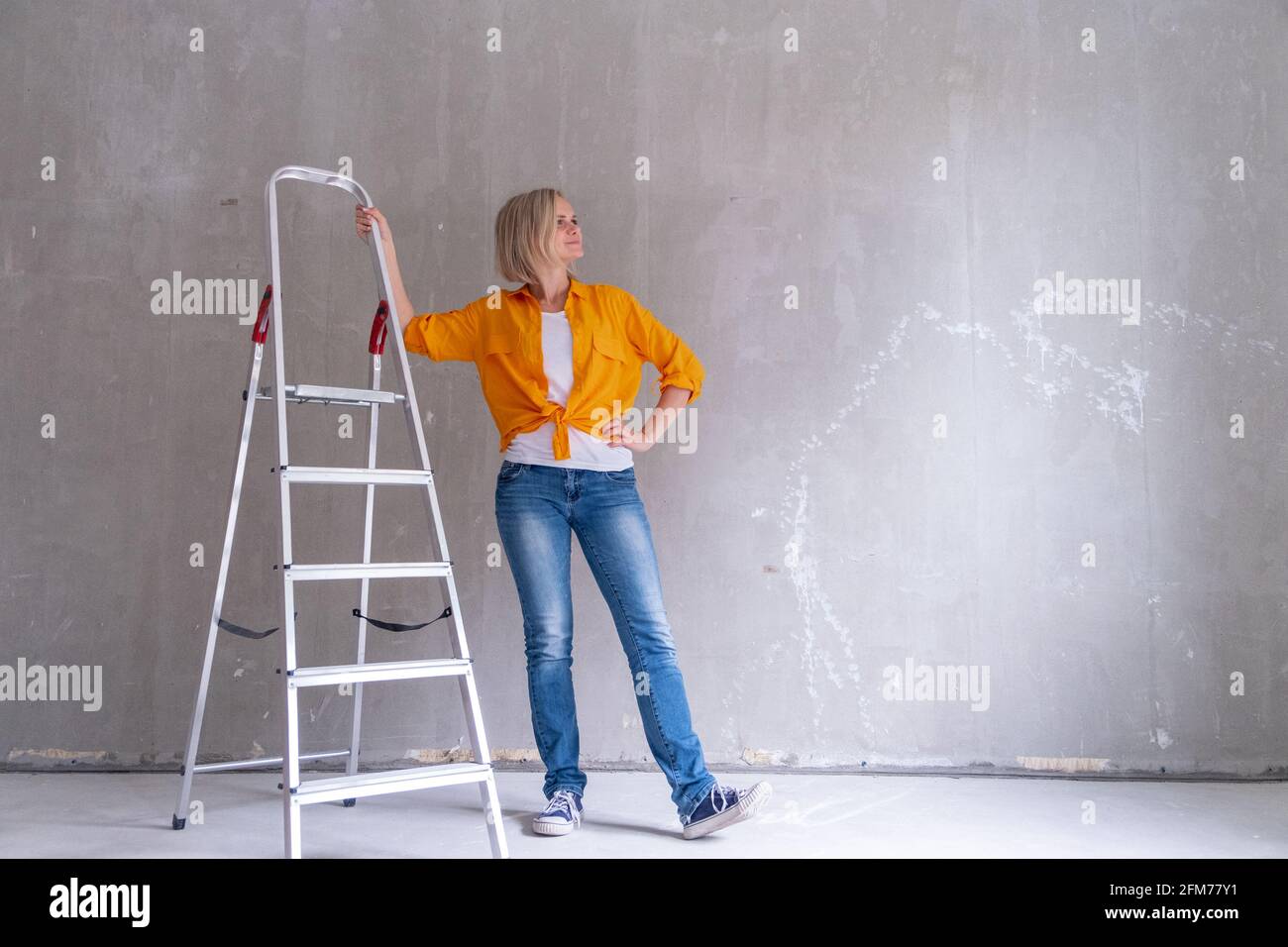 Appartamento di ristrutturazione. Donna felice si siede sulle scale vicino a muro vuoto a casa. Muro libero, ripara casa con le proprie mani. CopySpace per il testo. Foto Stock