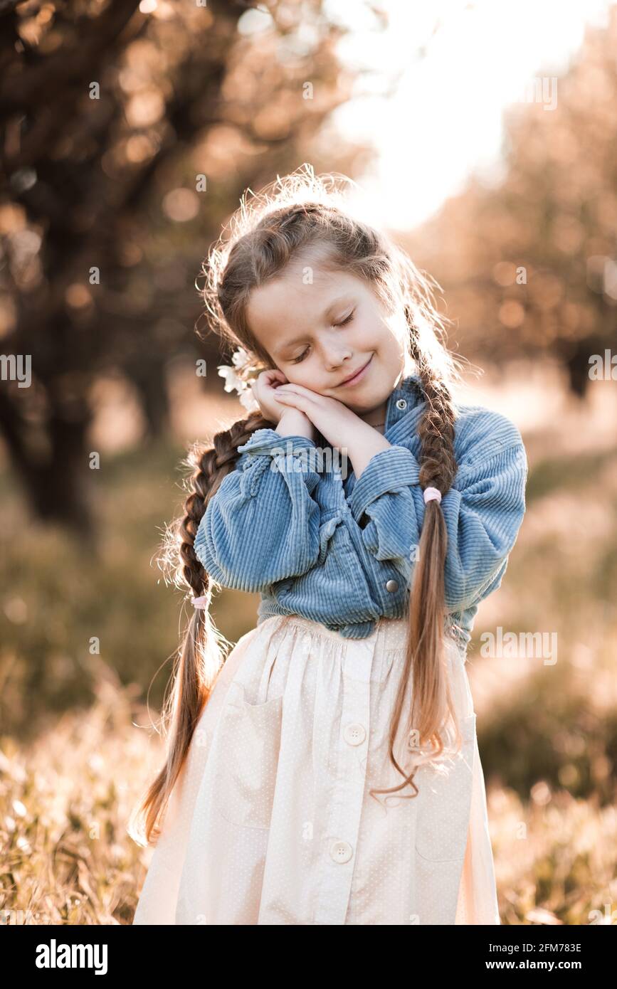 Sorridente ragazza bionda bambino 4-5 anni indossando abiti casual alla moda riposante su sfondo naturale soleggiato con occhi rivestiti. Infanzia. Sesone primaverile. HAP Foto Stock