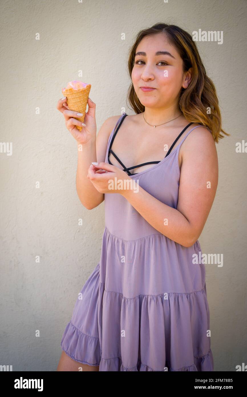 Petite giovane donna asiatica realisticamente mangiare Arcobaleno Sherbet gelato In un cono waffle in ambiente urbano Foto Stock