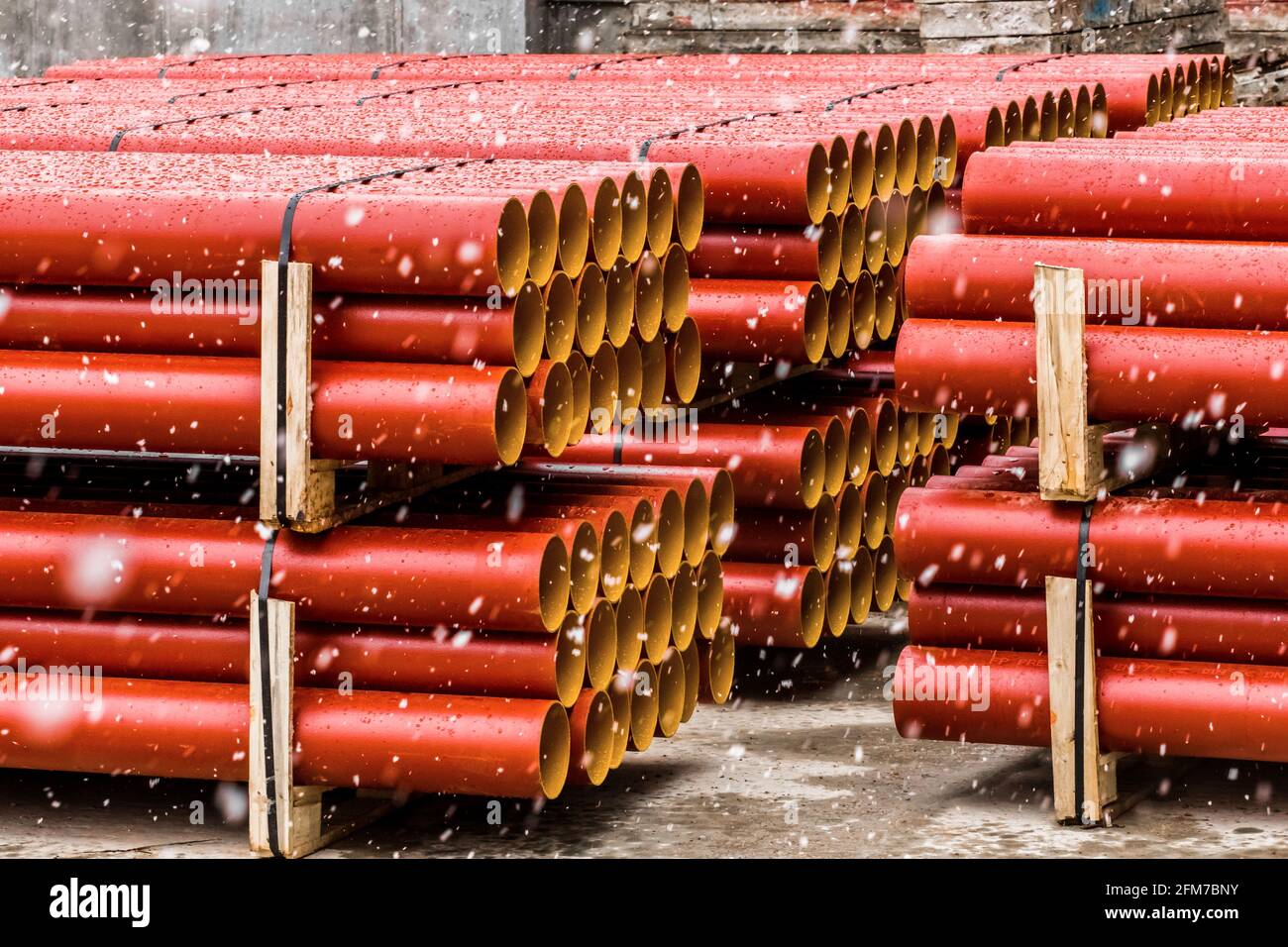 Cumulo di tubi termoplastici in polietilene industriale rotondi stoccaggio all'aperto in un cantiere con neve in inverno freddo. Foto Stock