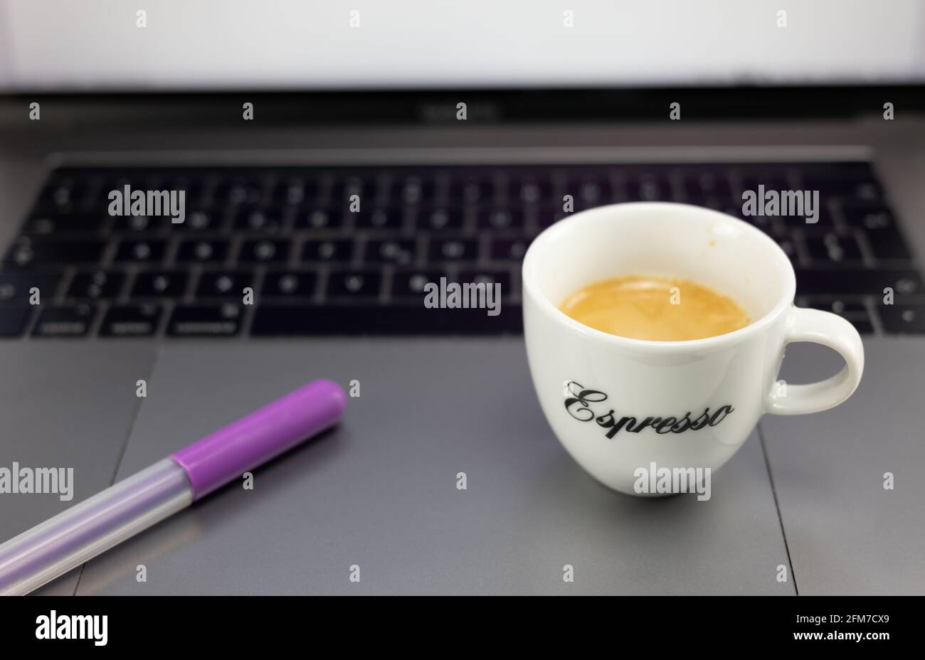 Una tazza di caffè espresso e una penna viola colorata sul computer desktop. Il concetto di pausa caffè in ufficio. Foto Stock
