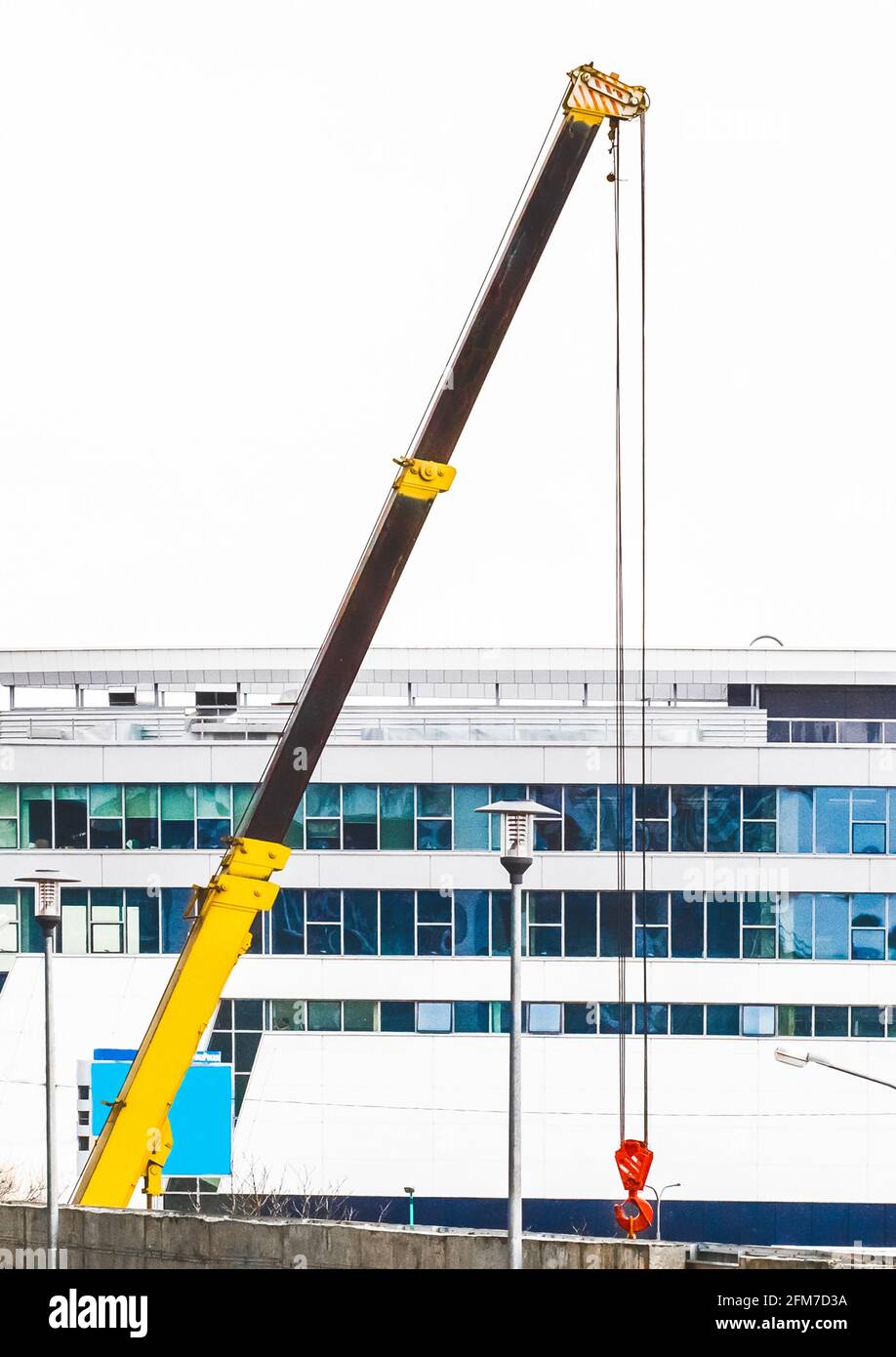 Attrezzature industriali per gru di sollevamento a macchina in cantiere sullo sfondo di una nuova e moderna facciata di un edificio urbano Foto Stock