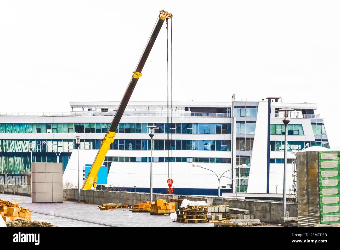 Attrezzature industriali per gru di sollevamento a macchina in cantiere sullo sfondo di una nuova e moderna facciata di un edificio urbano Foto Stock