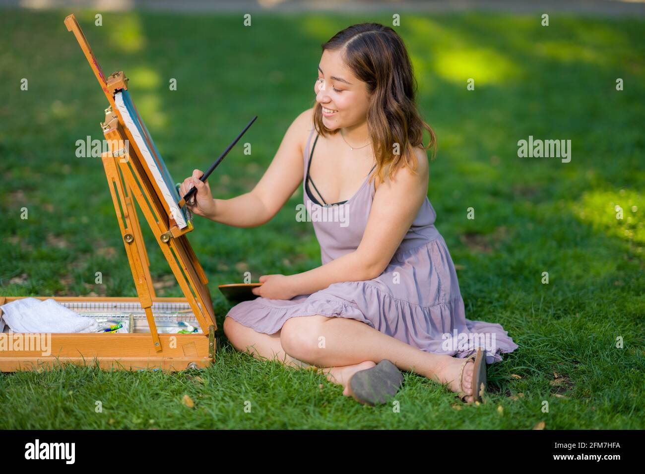Petite giovane donna asiatica studente Pittura nel Parco utilizzando Un armadietto Easel Foto Stock