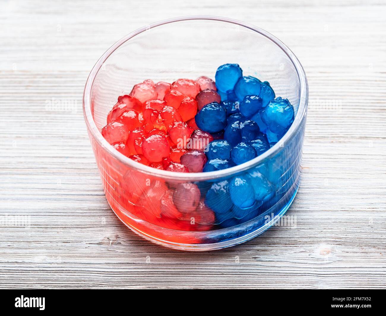 palle di tapioca bollite di colore rosso e blu in una ciotola di vetro su tavolo di legno grigio Foto Stock
