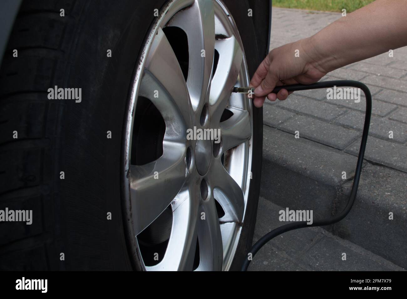 Una donna che sbatte sul marciapiede di un parcheggio stradale pavimentato grigio pompa la ruota anteriore nera pneumatico di una macchina blu chiaro da un compressore nero. Conce Foto Stock