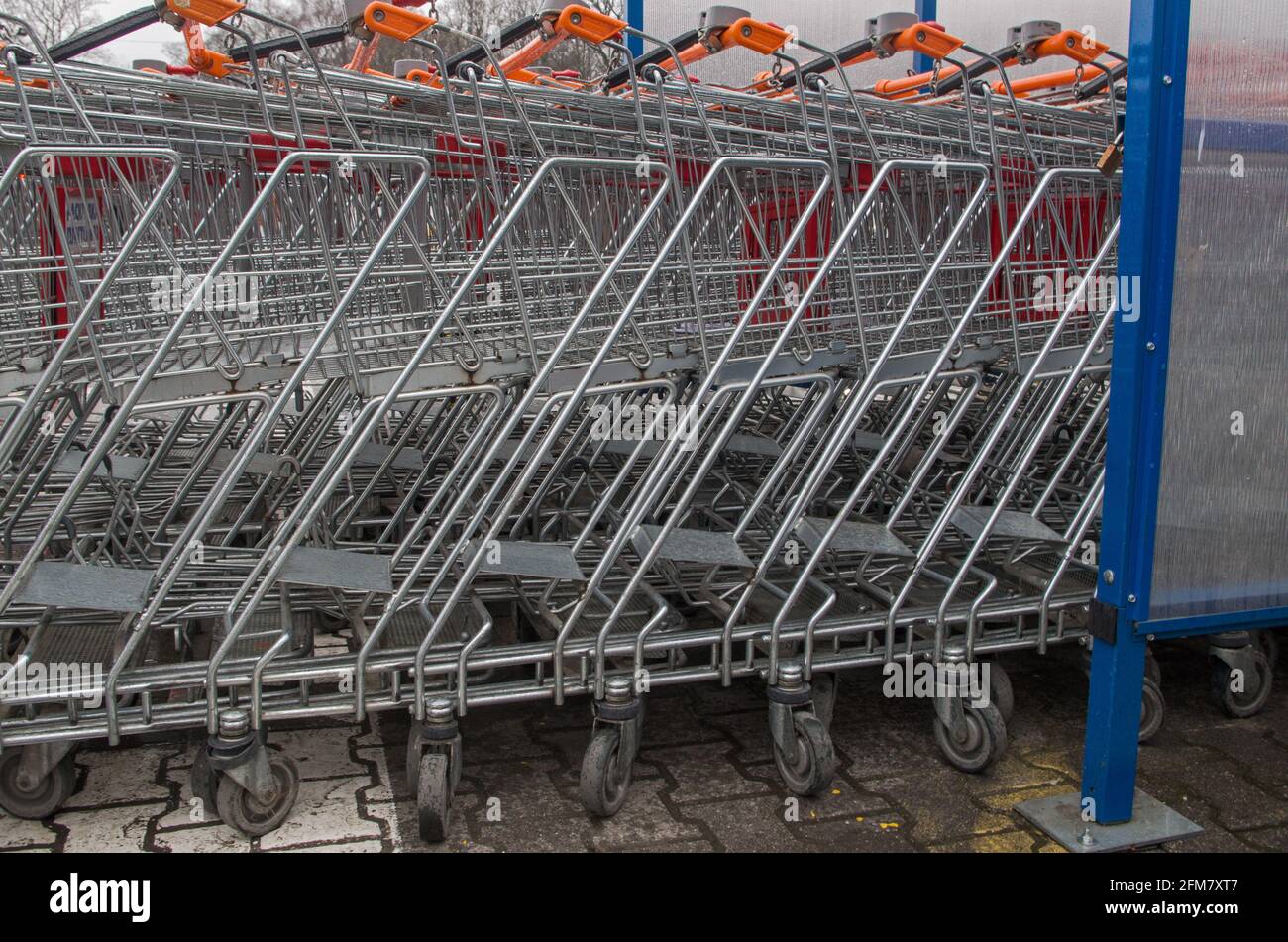 Fila di carrelli per la spesa in metallo con maniglie arancioni in posizione stretta Uno in un altro all'aperto di fronte al negozio fai da te in luogo appositamente designato sul c piovoso Foto Stock