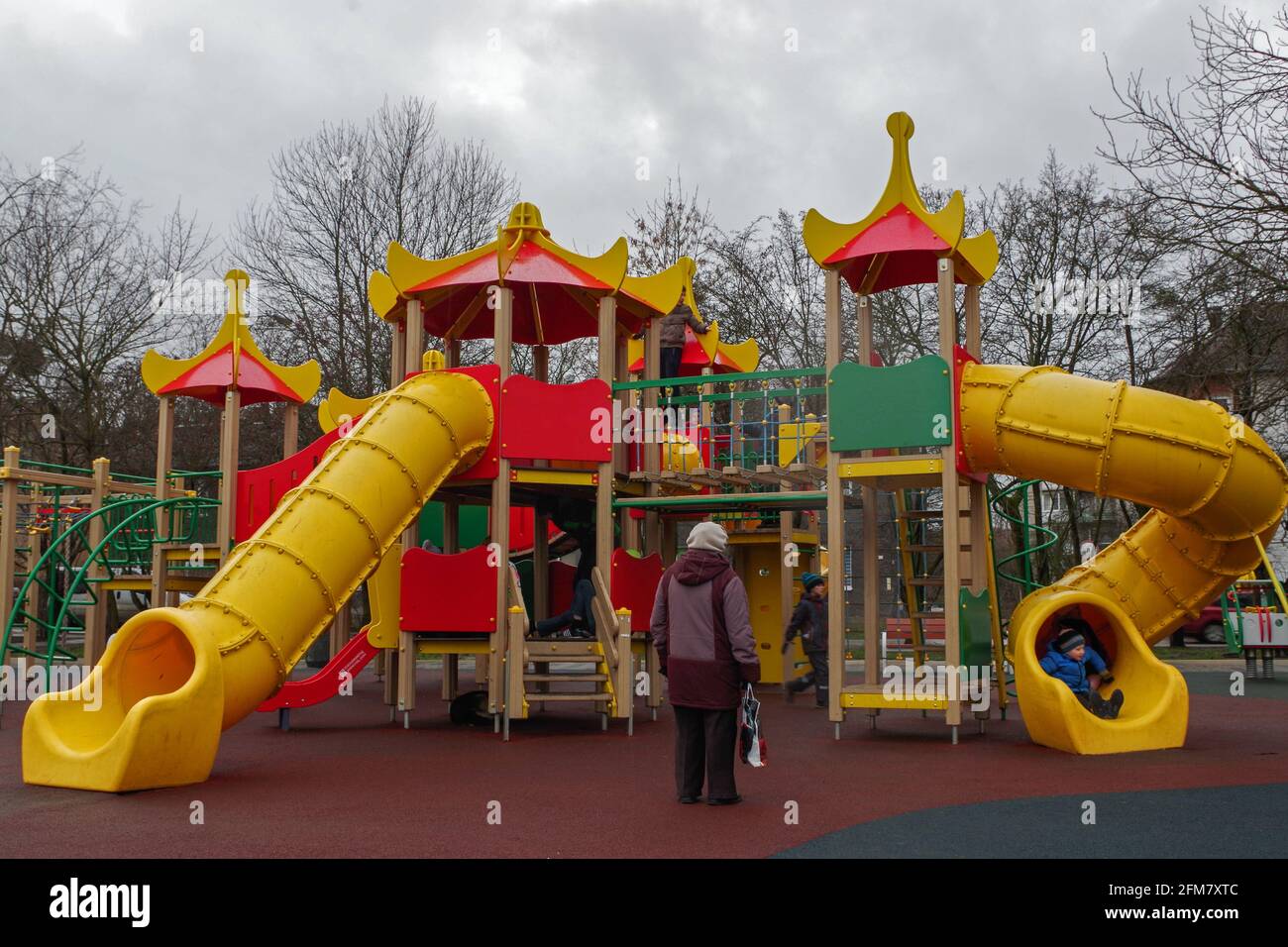 Parco giochi è un complesso di torri con tetti rossi collegati da piattaforme con tubi gialli-scivoli con i bambini che si divertono su di esso e nonna in attesa Foto Stock
