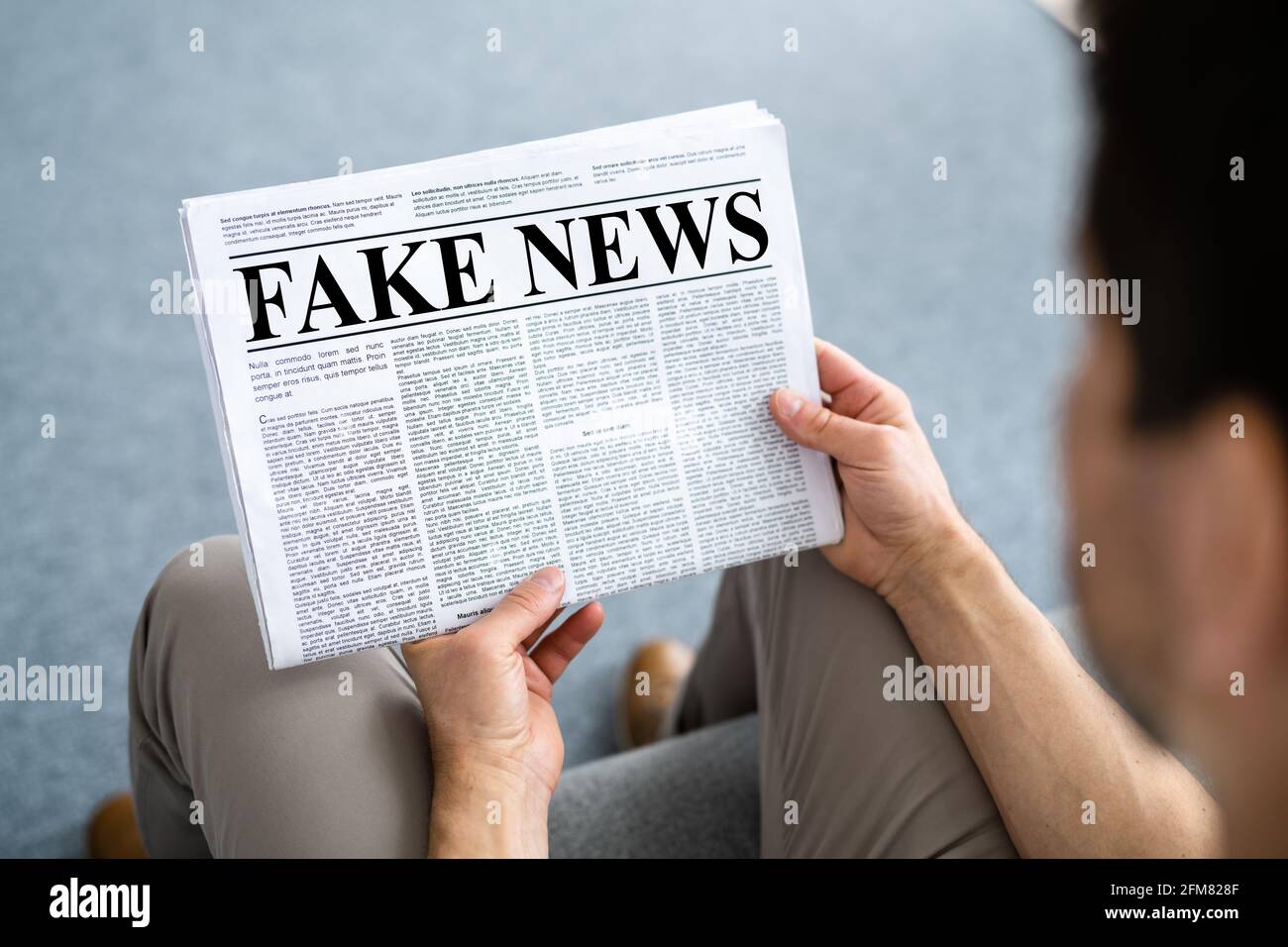 Uomo d'affari che legge l'articolo di notizie del fiocco sul giornale in soggiorno Foto Stock