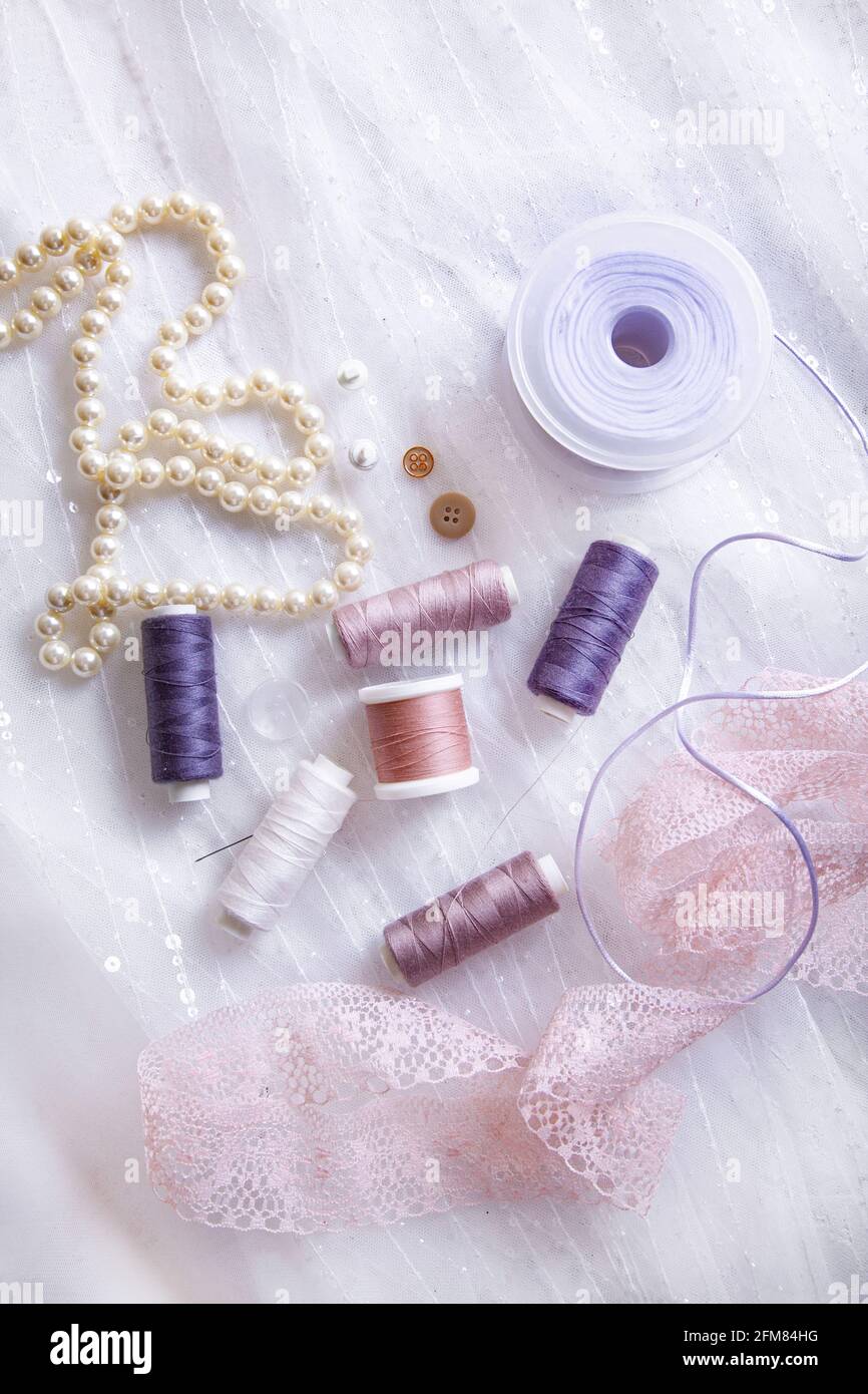 Articoli per la sartoria - bobine di filo, aghi, nastri, lacci, bottoni, collana di perle su uno sfondo di tulle con paillettes. Foto Stock