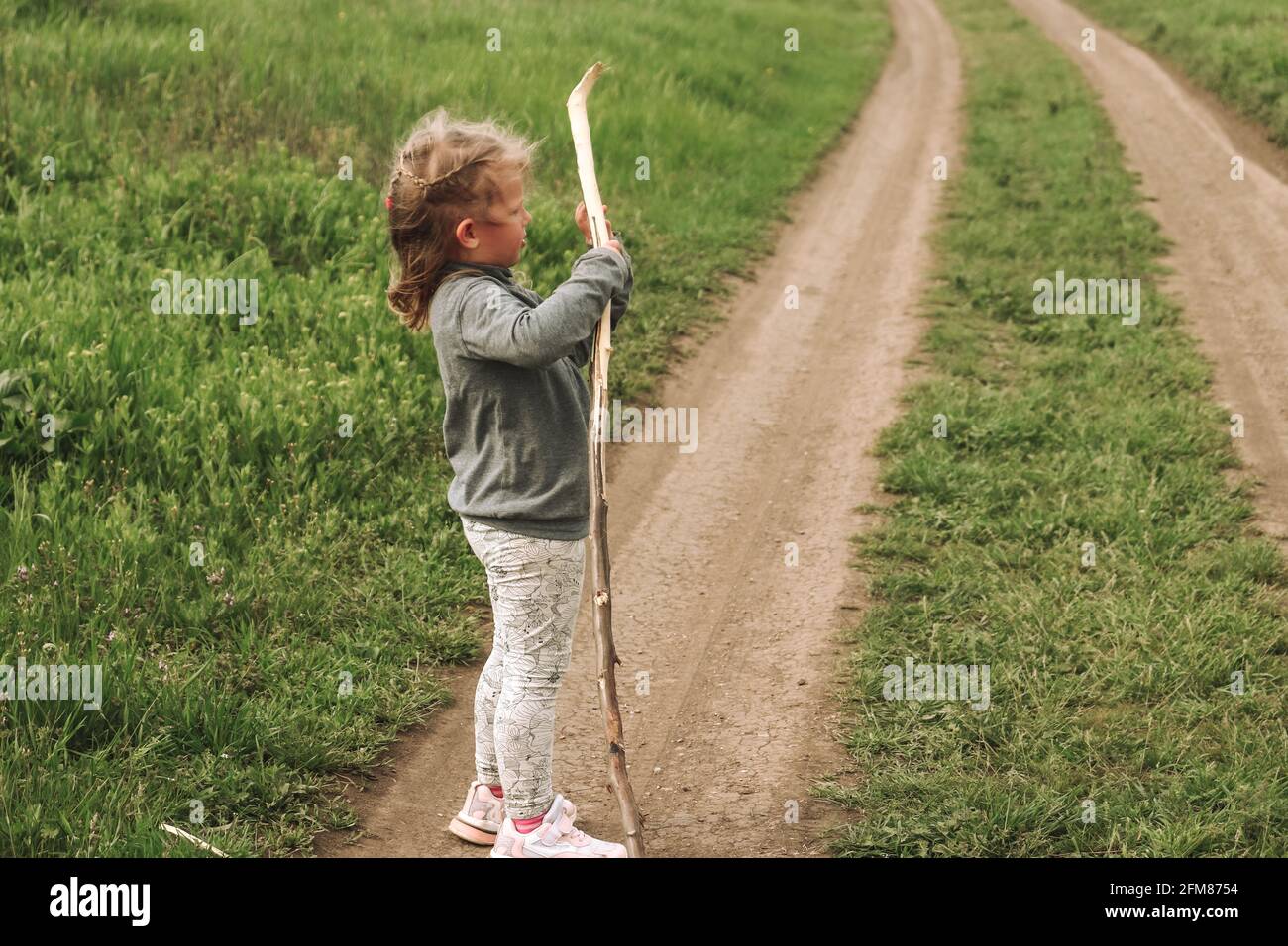 Il bambino gioca con un bastone di albero. Ritratto dei bambini. Ragazza bionda 4 anni. Umana e natura. Il bambino gioca in natura. Foto Stock