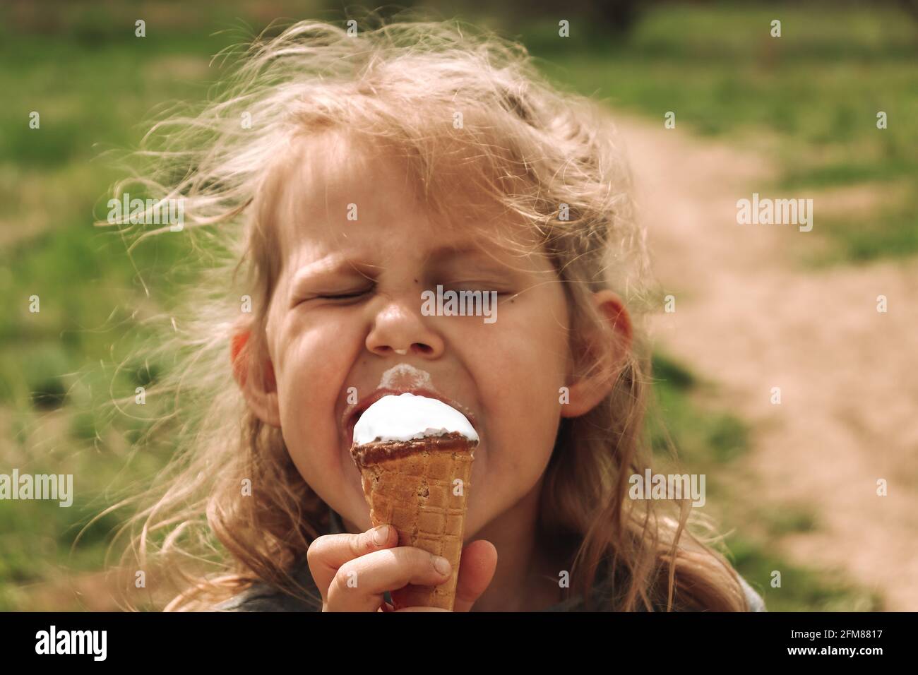 Ritratto di un bambino in natura. Spazio di copia. Bella ragazza bionda di 4 anni. Sfondo verde erba. Il bambino sta mangiando gelato freddo. Foto Stock