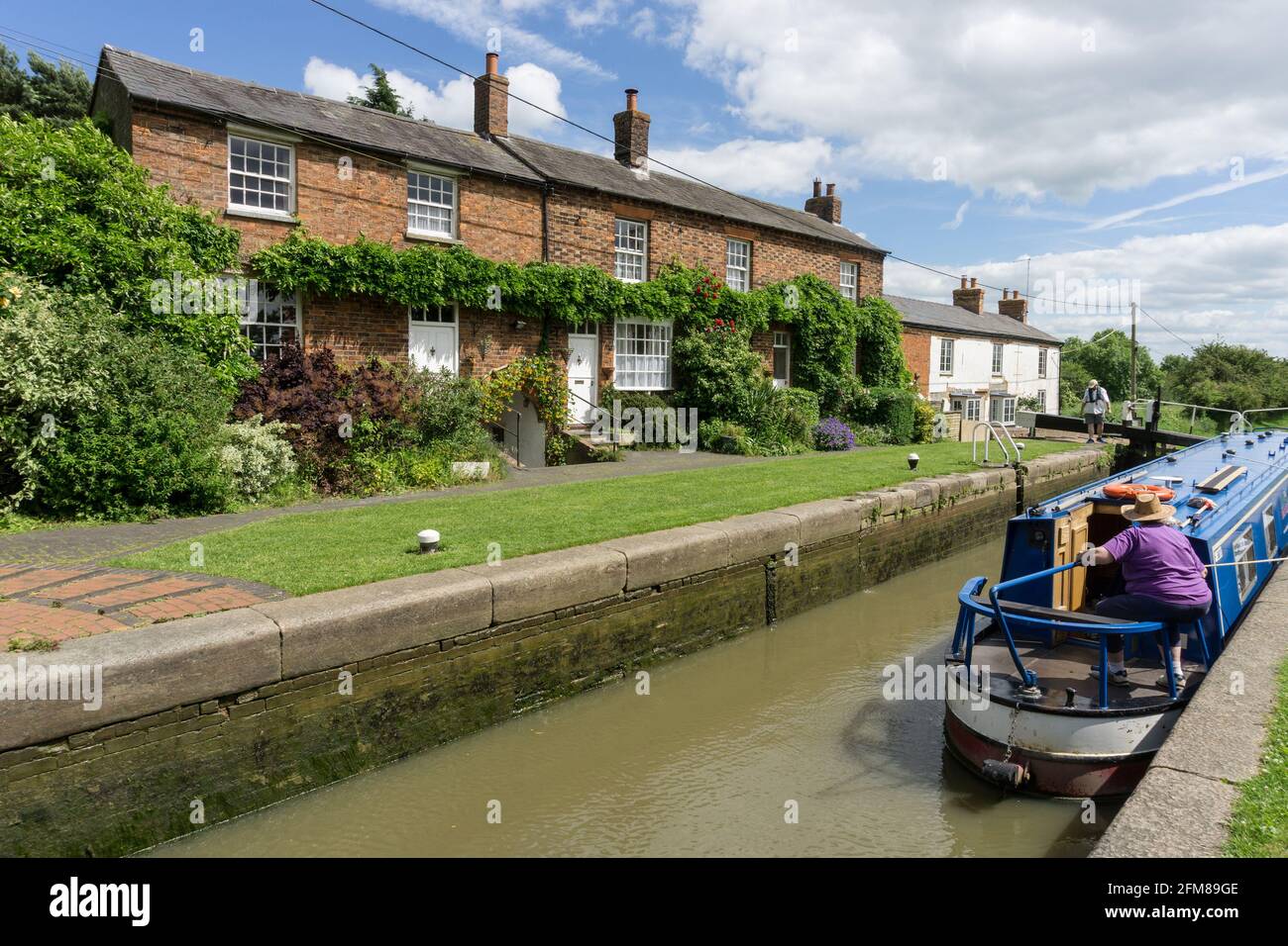 Narrowboat e porte di blocco sul canale Grand Union, Whilton serrature, Northamptonshire, UK; case sul canale sullo sfondo Foto Stock
