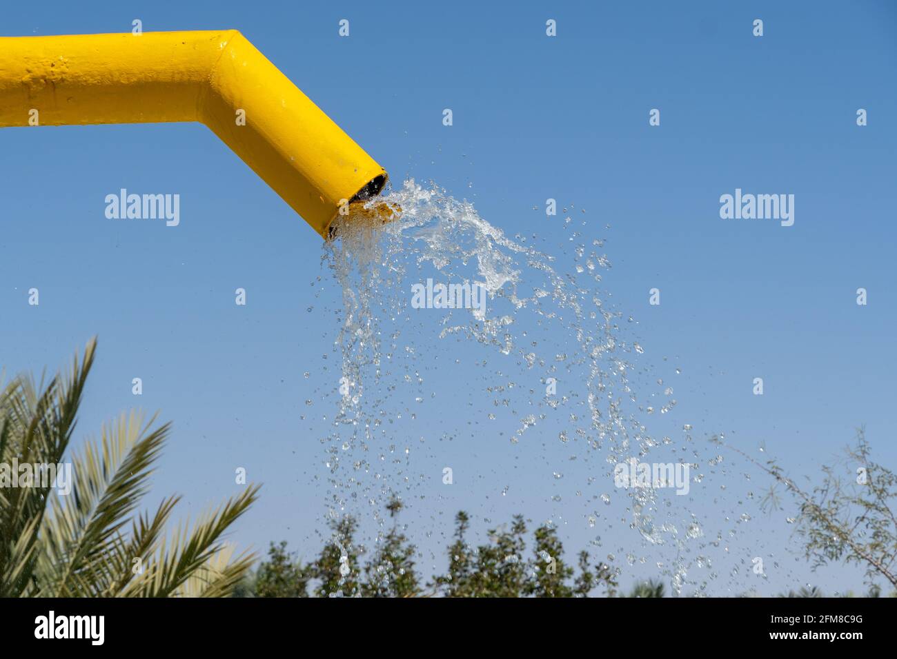 Acqua che cade dalla fontana gialla di colore luminoso alla piscina sotto. Copia spazio a destra. Foto Stock